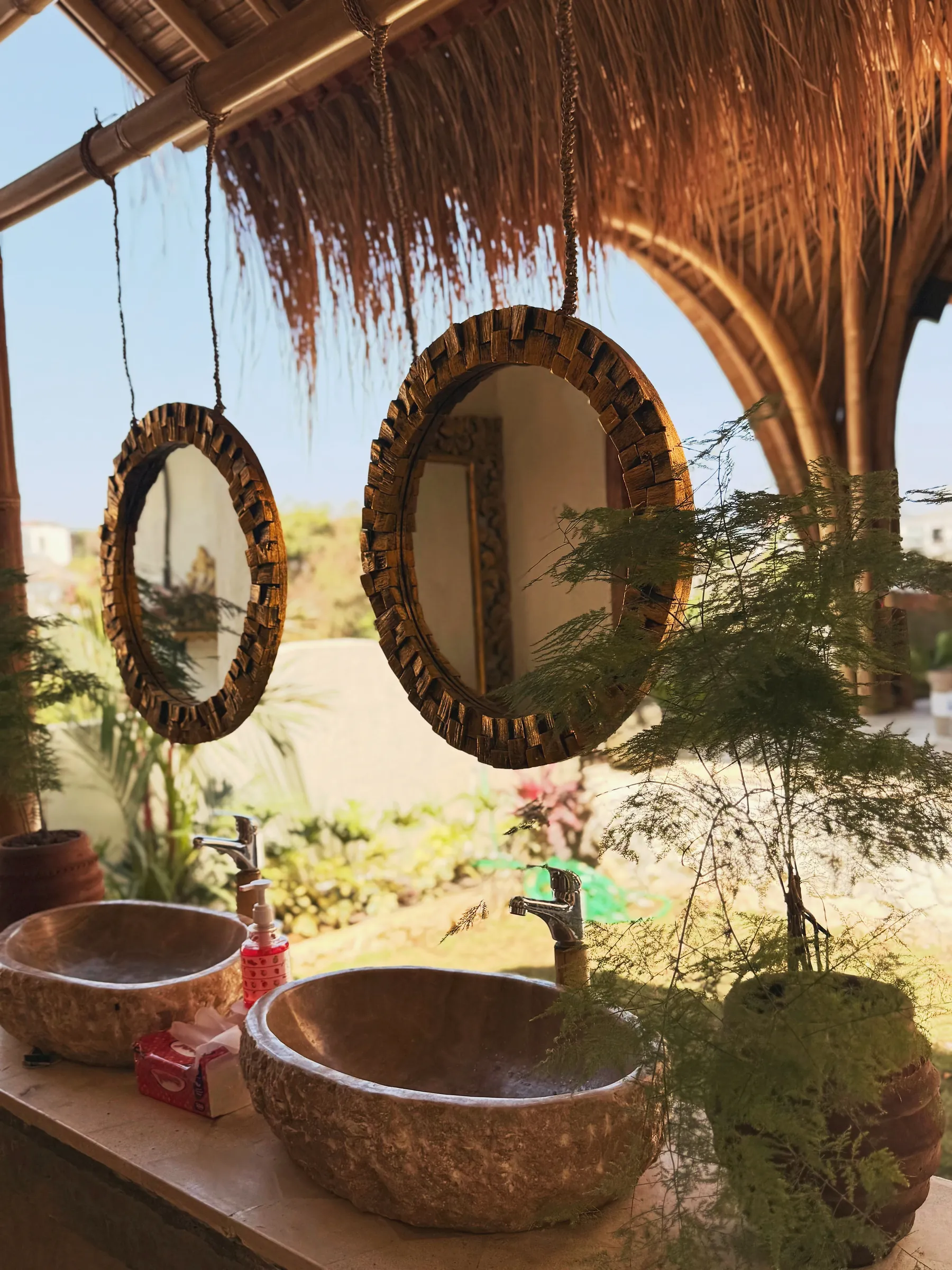 Carved stone basins and round wooden mirrors under a thatched roof
