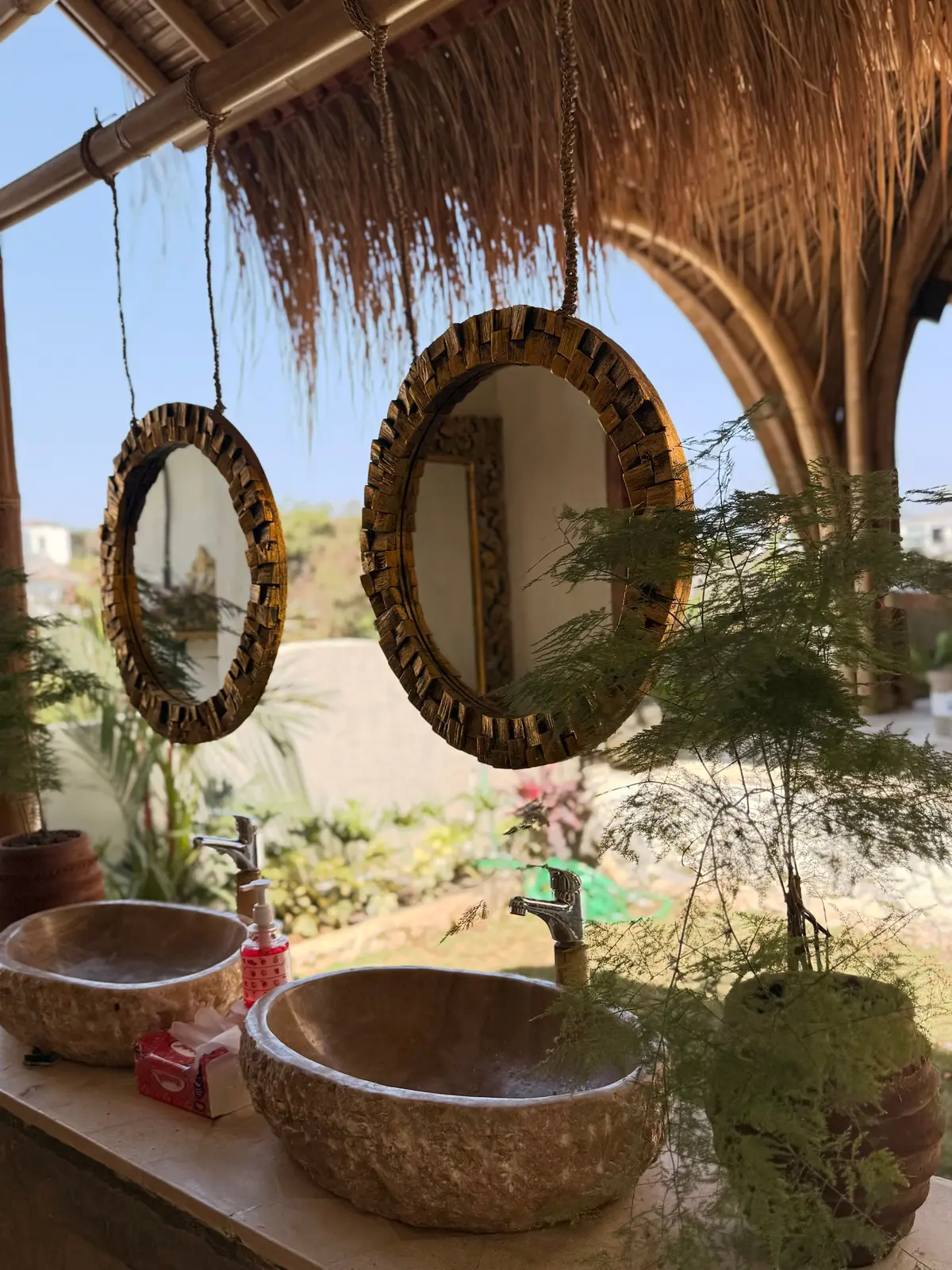 Carved stone basins and round wooden mirrors under a thatched roof