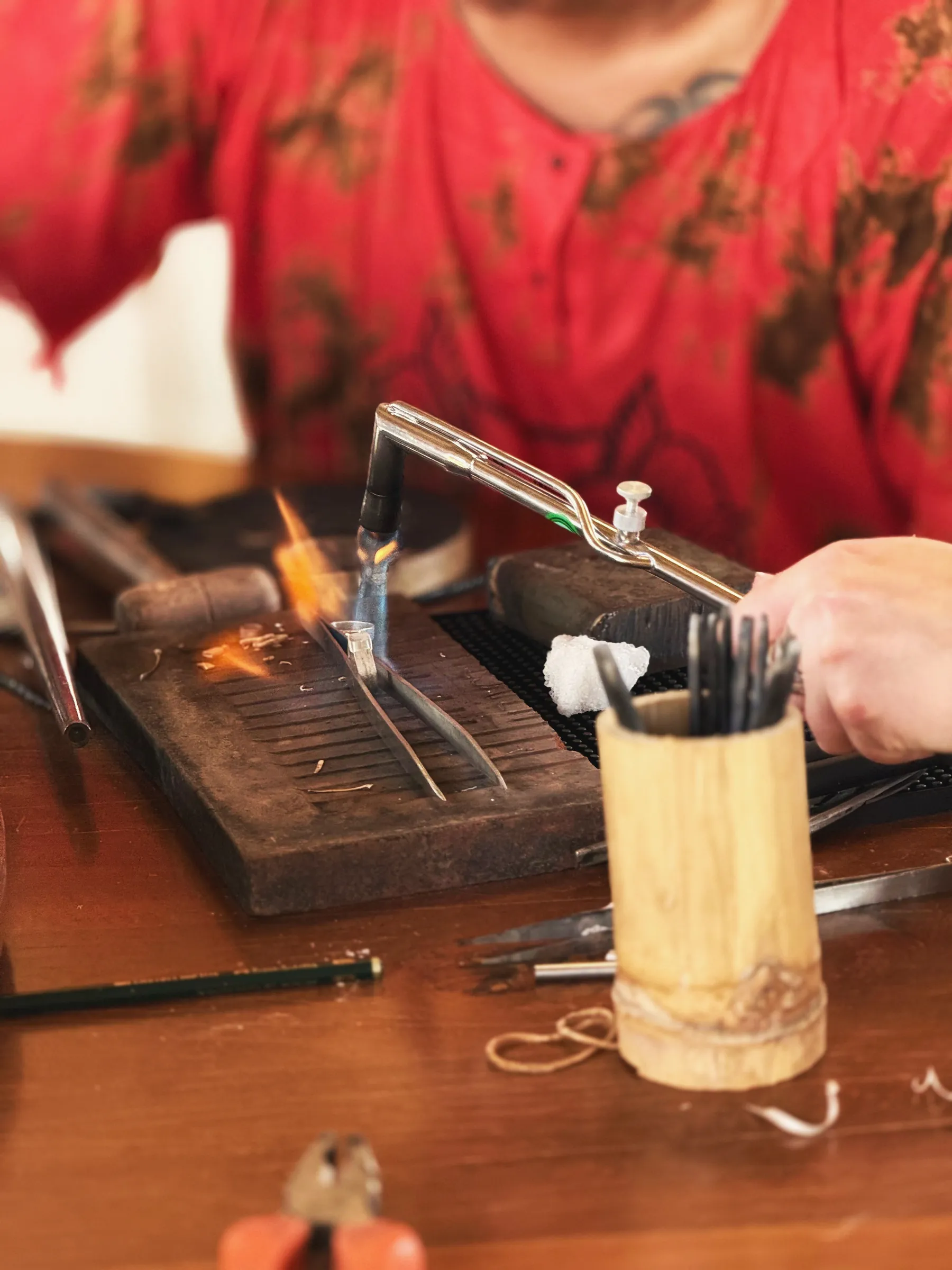 A torch flame on the soldering block beside a bamboo tool cup